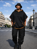 Person wearing a black hooded outfit with orange accents on a city street.
