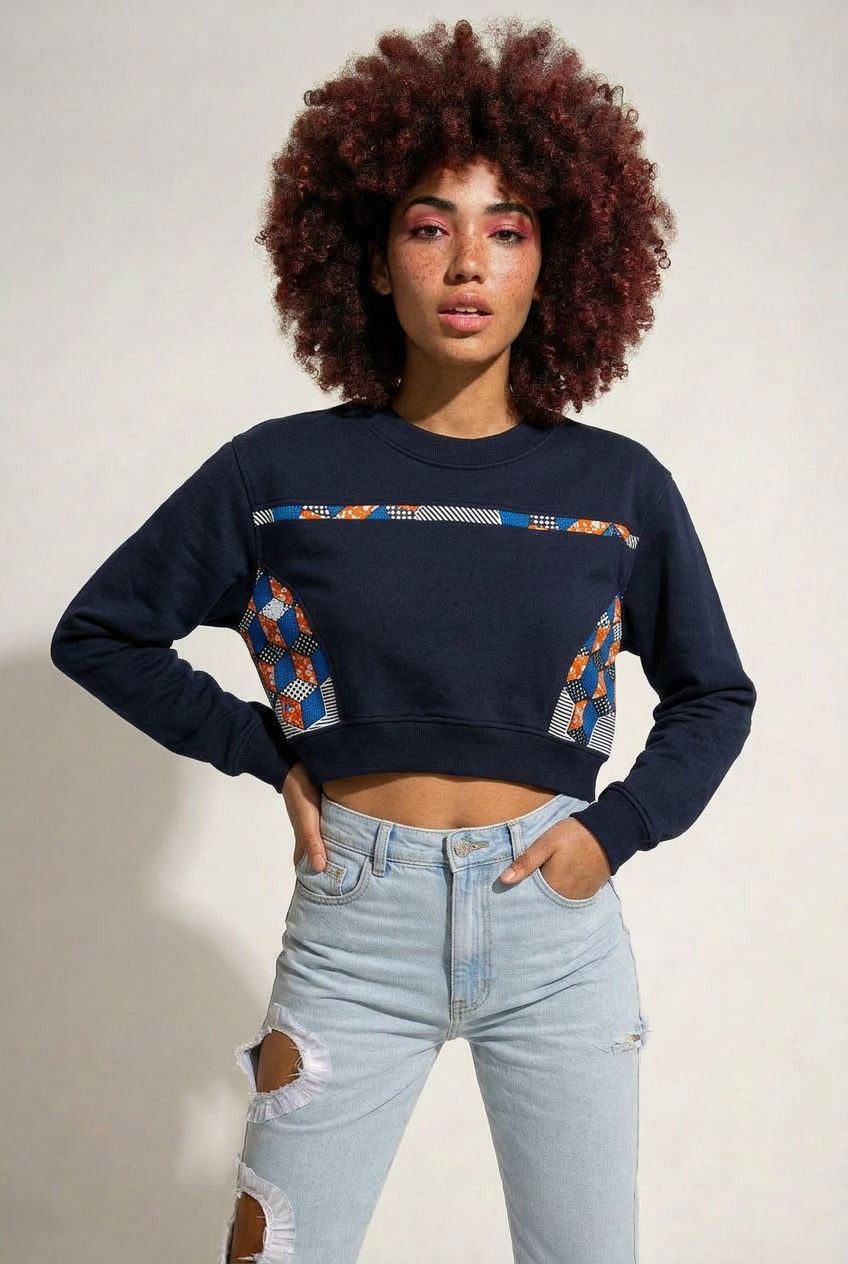 Person wearing a black sweatshirt with colorful patterns and light blue jeans on a plain background