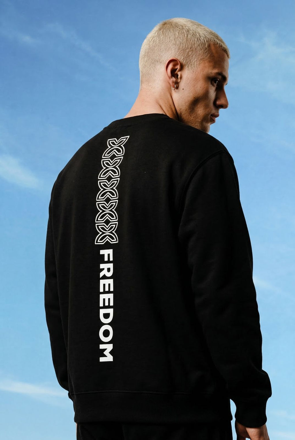 Person wearing a black sweatshirt with 'FREEDOM' printed on the back against a blue sky.