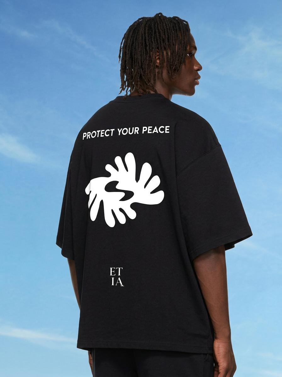 Person wearing a black t-shirt with 'Protect Your Peace' text and white graphic design against a blue sky.