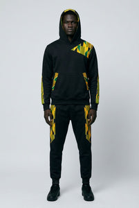 Person wearing a black hoodie and pants with yellow and green patterns on a white background